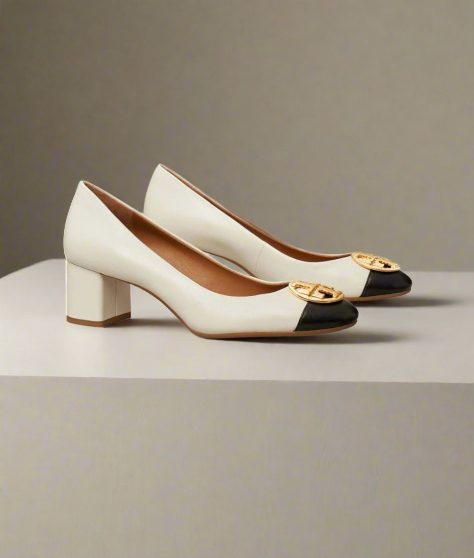 Pair of white and black high-heeled shoes with gold accents on a light gray background