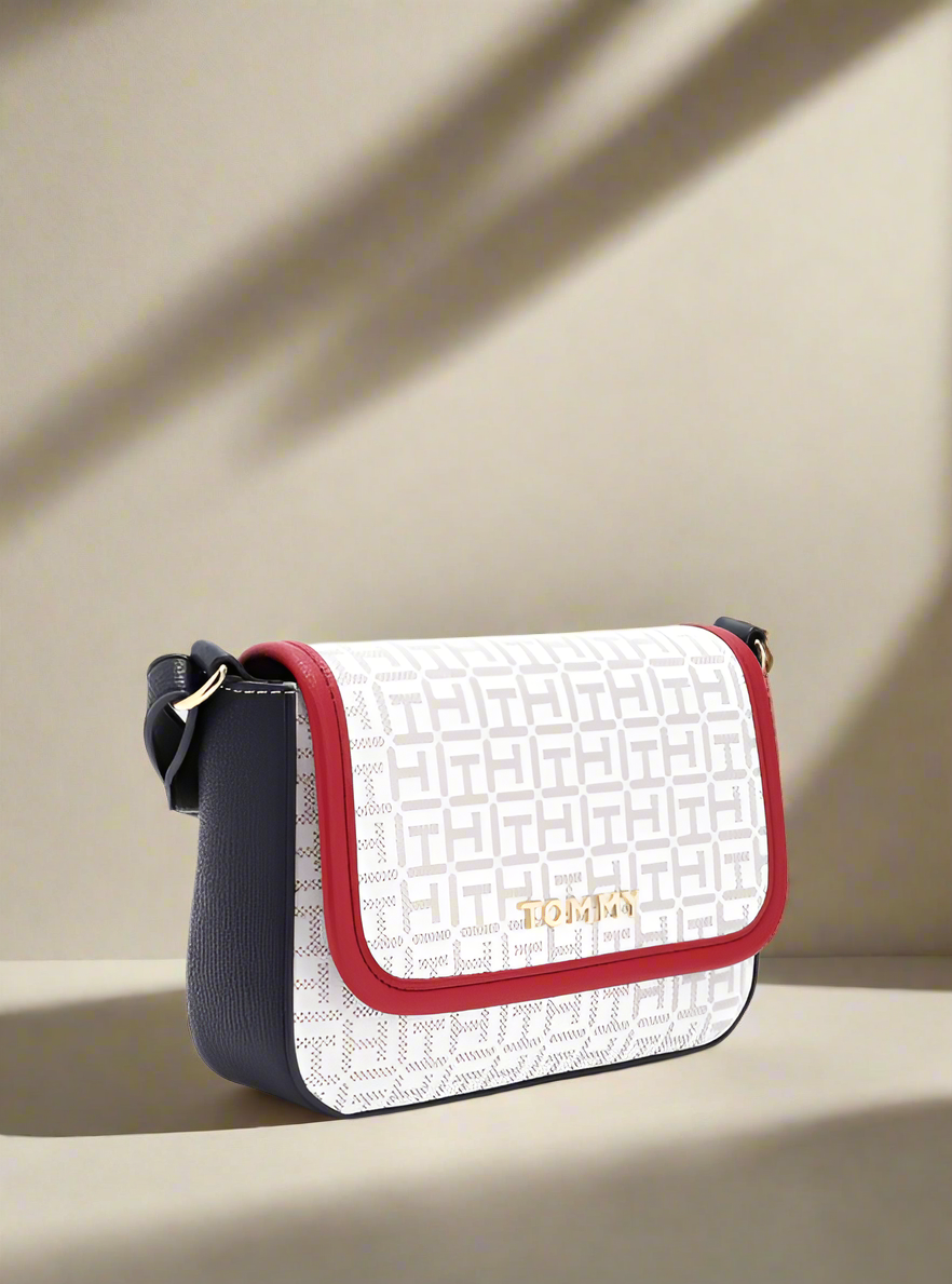 White crossbody bag with red accents and gold logo on a light gray background