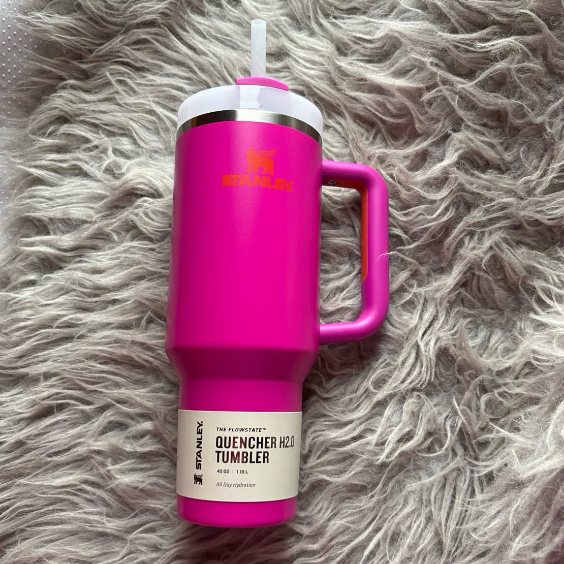 Pink Stanley tumbler with handle on a fluffy gray surface