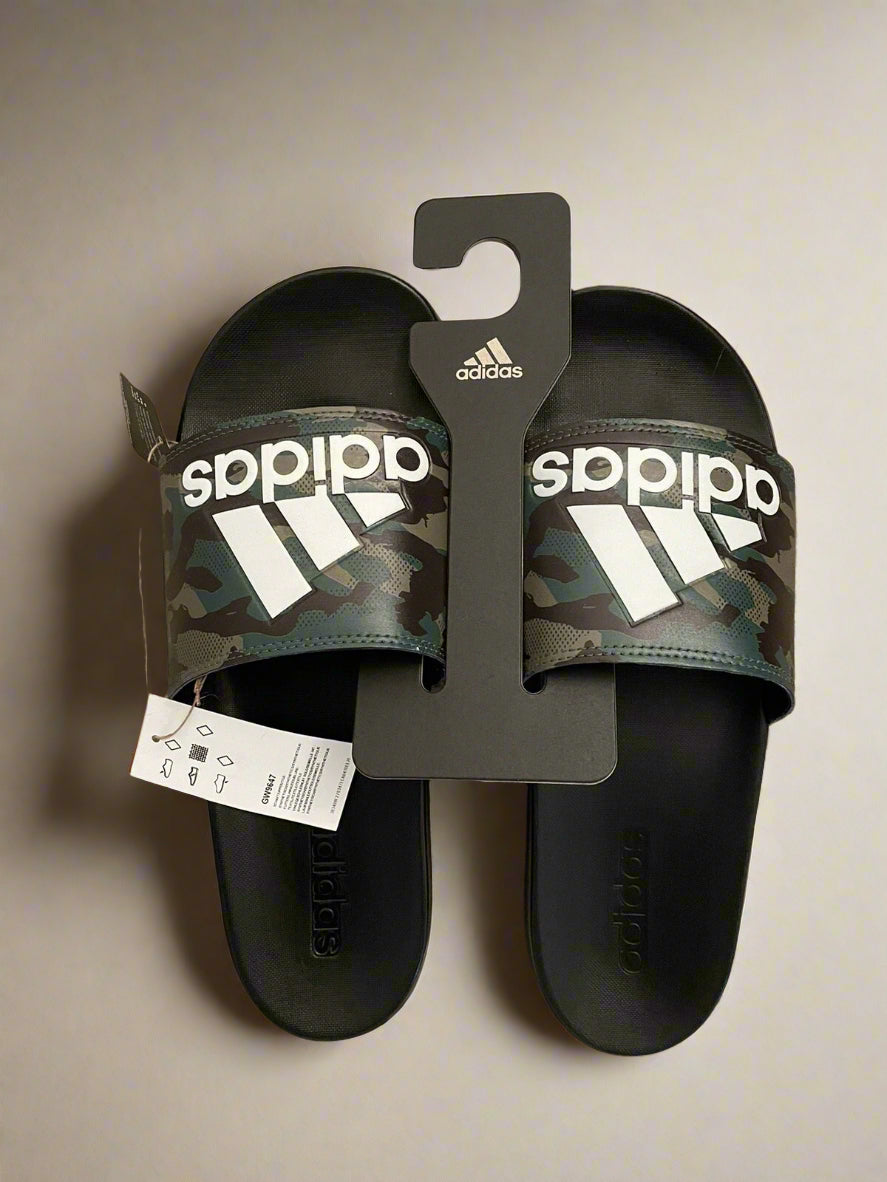 Pair of black Adidas slides with camouflage pattern on a beige carpet